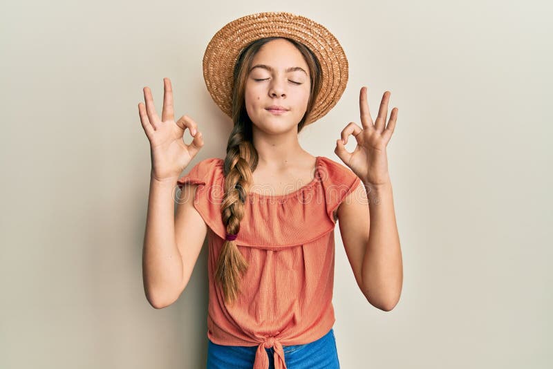 Bella morena pequeña niña con sombrero de verano relajarse y sonreír con los ojos cerrados haciendo gesto de meditación con los de fotos de archivo libres de regalías