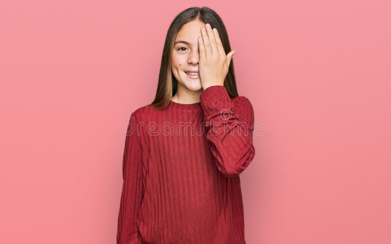 Bella morena pequeña niña con suéter casual cubriendo un ojo con sonrisa de confianza en la mano en la cara y emoción sorpresa foto de archivo libre de regalías