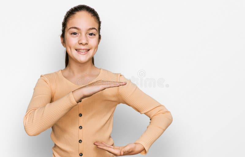 Bella morena pequeña niña con suéter casual gesto con manos que muestran un símbolo de gran tamaño y gran tamaño fotos de archivo