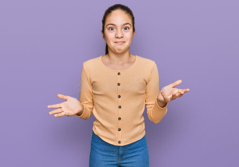 Bella morena pequeña niña con suéter casual sin idea y expresión confusa con brazos y manos levantados foto de archivo libre de regalías