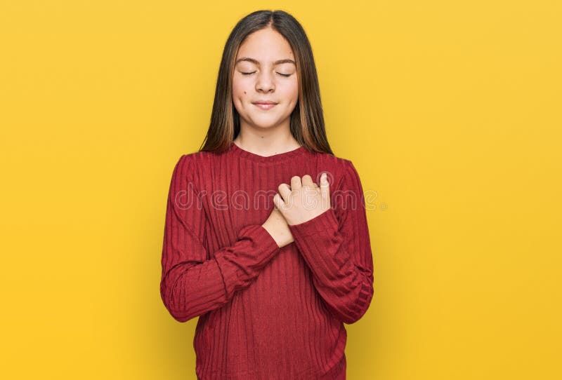 Bella morena pequeña niña con suéter casual sonriendo con las manos en el pecho con los ojos cerrados y gesto agradecido en la car imagen de archivo libre de regalías