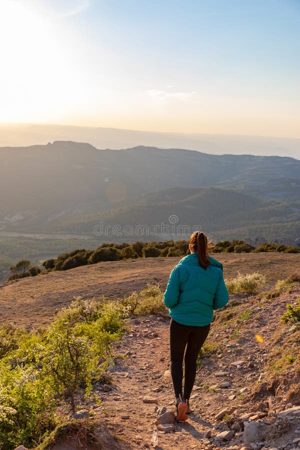 Bella mujer caminando por un sendero durante la puesta de sol con montañas en el fondo fotos de archivo libres de regalías
