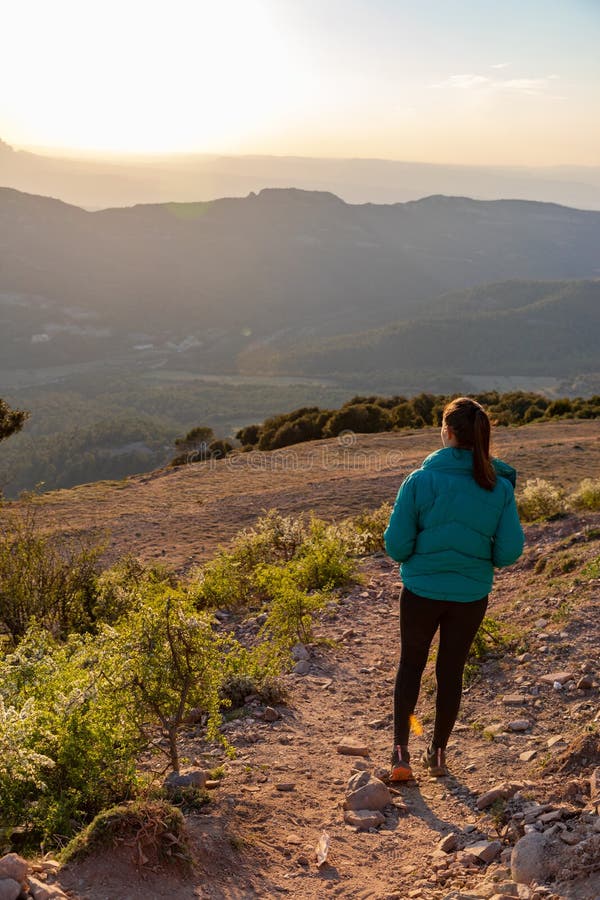Bella mujer caminando por un sendero durante la puesta de sol con montañas en el fondo imagen de archivo