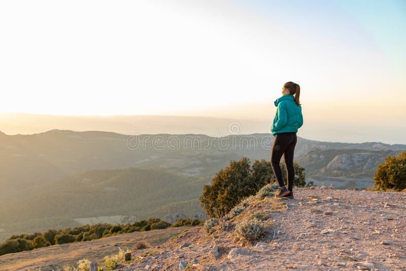 Bella mujer de pie al borde durante la puesta de sol con montañas al fondo foto de archivo