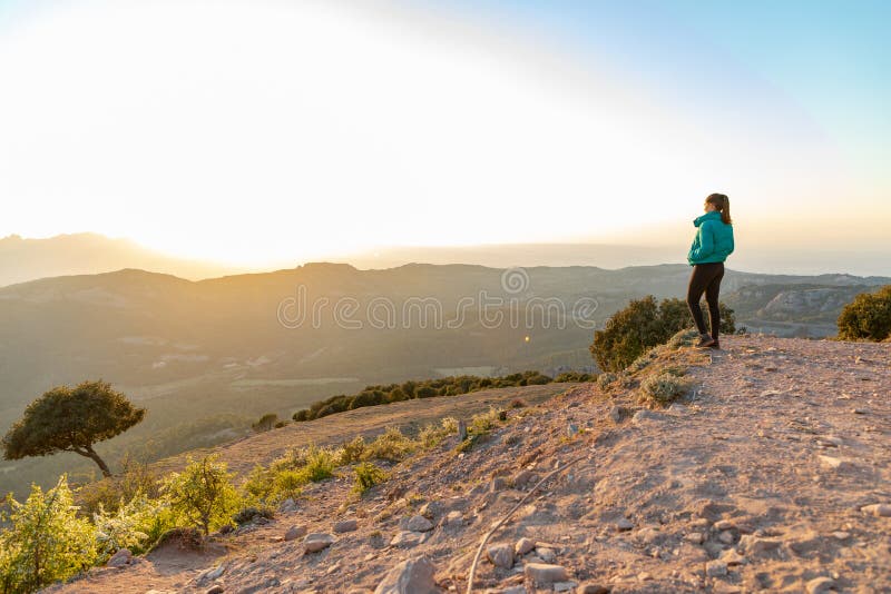 Bella mujer de pie al borde durante la puesta de sol con montañas al fondo foto de archivo libre de regalías