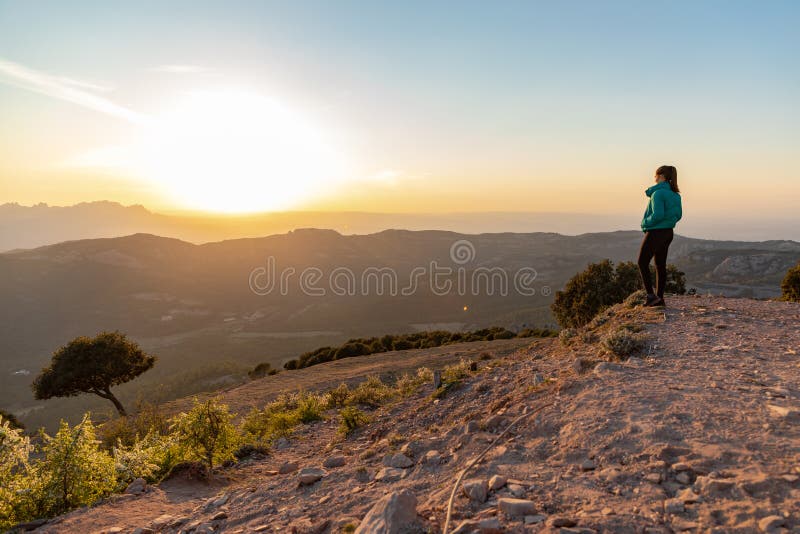 Bella mujer de pie al borde durante la puesta de sol con montañas al fondo imágenes de archivo libres de regalías