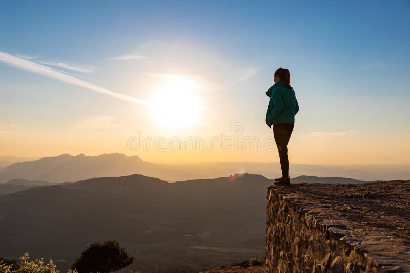 Bella mujer de pie al borde durante la puesta de sol con montañas al fondo fotografía de archivo libre de regalías