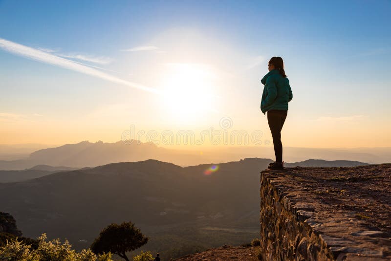 Bella mujer de pie al borde durante la puesta de sol con montañas al fondo foto de archivo