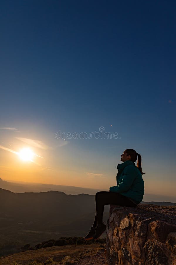 Bella mujer sentada al borde durante la puesta de sol con montañas imagenes de archivo
