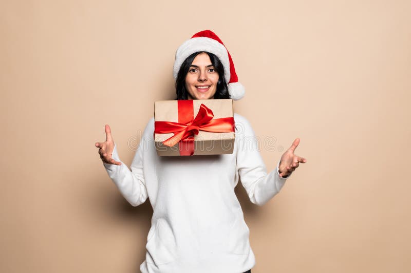 Bella mujer sostiene regalo sobre fondo beige. sombrero santa. retrato de chica navideña fotografía de archivo