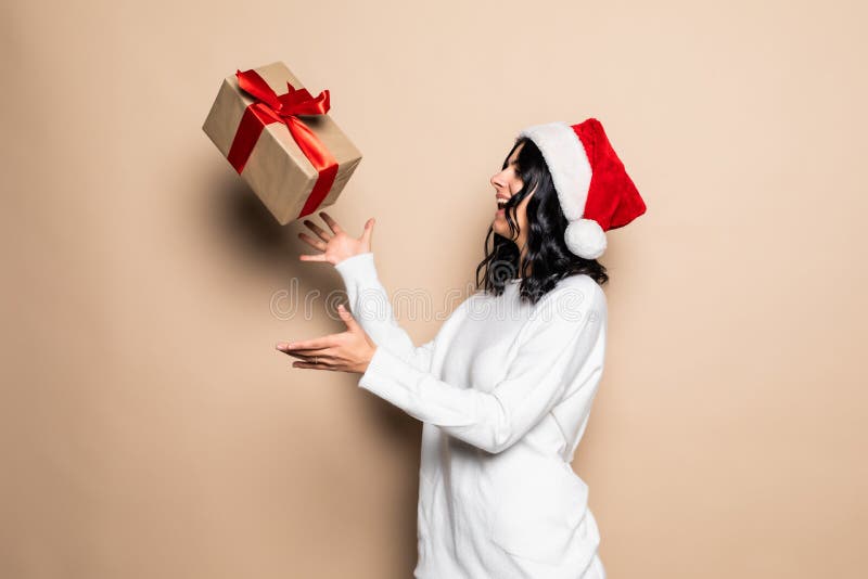 Bella mujer sostiene regalo sobre fondo beige. sombrero santa. retrato de chica navideña fotos de archivo libres de regalías