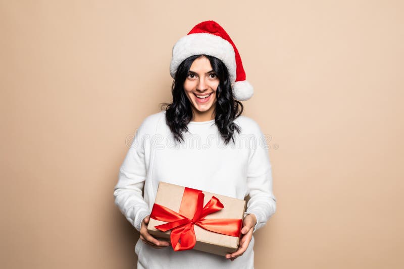 Bella mujer sostiene regalo sobre fondo beige. sombrero santa. retrato de chica navideña fotos de archivo