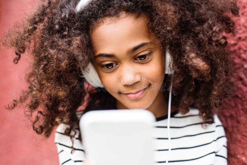 Bella ragazza afroamericana con lo Smart Phone e le cuffie fotografia stock libera da diritti Bella ragazza afroamericana con lo Smart Phone e le cuffie fotografia stock libera da diritti