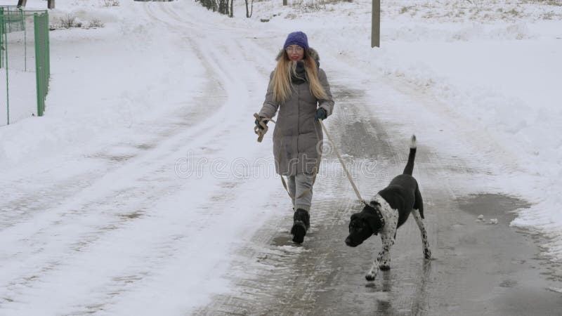 Bella ragazza allegra che cammina il puntatore del cane nella neve
