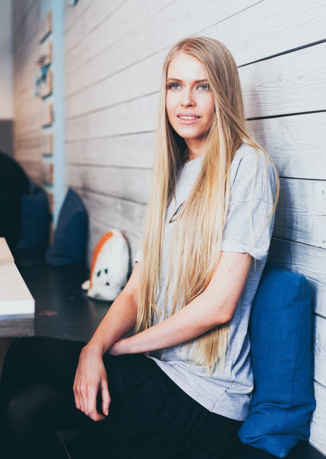 Bella ragazza bionda alla moda con capelli lunghi che si siedono ad una tavola in un caffè alla moda dei pantaloni a vita bassa c immagine stock libera da diritti Bella ragazza bionda alla moda con capelli lunghi che si siedono ad una tavola in un caffè alla moda dei pantaloni a vita bassa c immagine stock libera da diritti