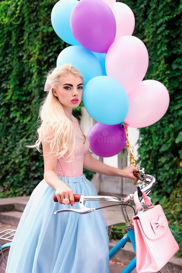Bella ragazza bionda che tiene i palloni luminosi mentre ciclando fotografia stock Bella ragazza bionda che tiene i palloni luminosi mentre ciclando fotografia stock
