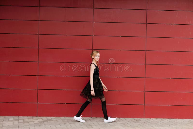 Bella ragazza bionda in un vestito nero che posa contro una parete rossa fotografia stock Bella ragazza bionda in un vestito nero che posa contro una parete rossa fotografia stock