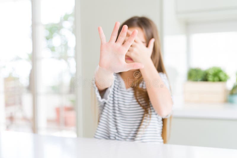 Bella ragazza che indossa una camicia a strisce che copre gli occhi con le mani e fa un gesto di arresto con espressione triste e fotografie stock