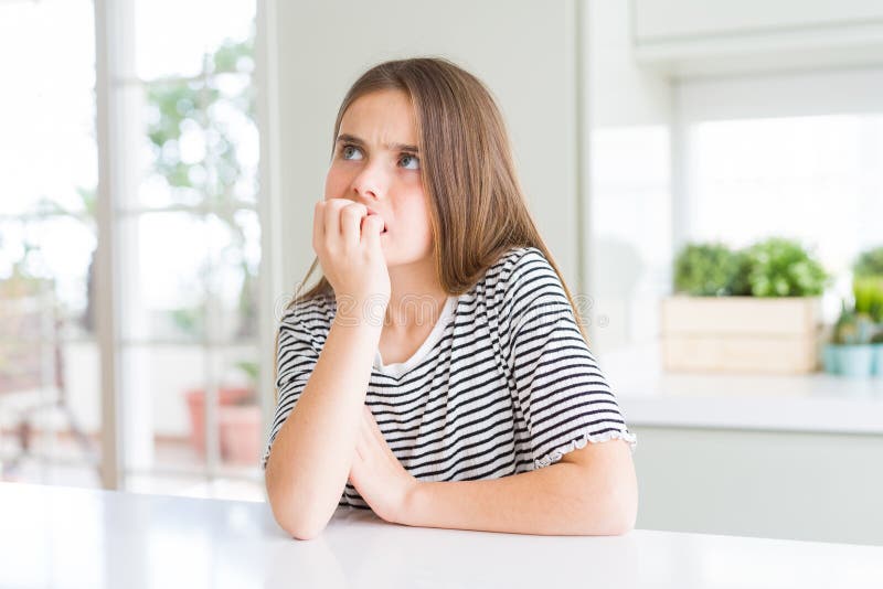 Bella ragazza che indossa una camicia a strisce che sembra stressata e nervosa con le mani sulle unghie morse fotografia stock libera da diritti