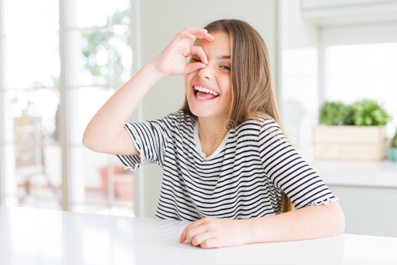 Bella ragazza che indossa una maglietta a strisce mentre fa un gesto d'accordo con la mano sorridente che guarda tra le dita con u fotografia stock libera da diritti