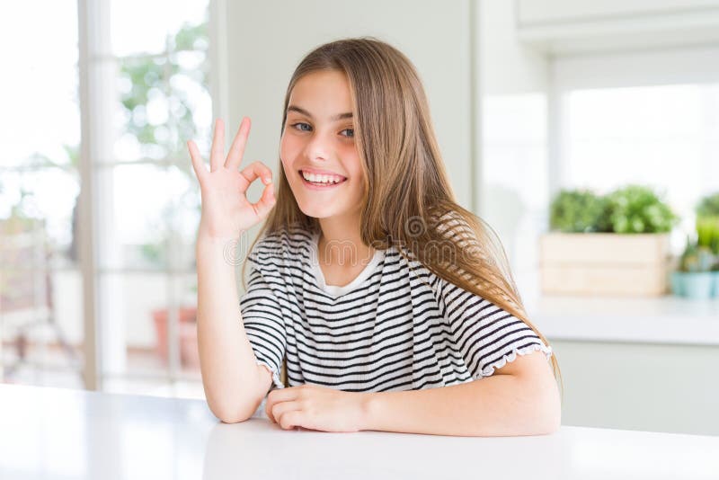 Bella ragazza che indossa una maglietta a strisce che sorride positivamente mentre fa un buon segno con la mano e le dita immagine stock libera da diritti