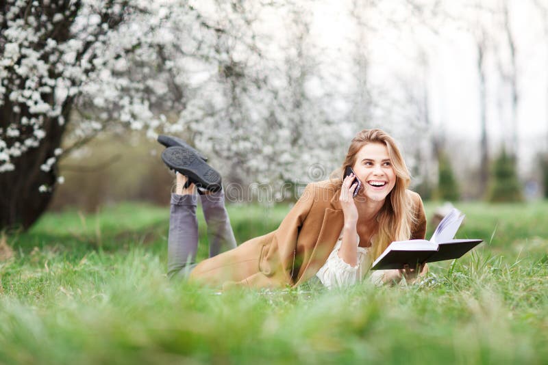 Bella ragazza che parla sul suo telefono nel giardino del fiore un giorno di molla immagini stock Bella ragazza che parla sul suo telefono nel giardino del fiore un giorno di molla immagini stock