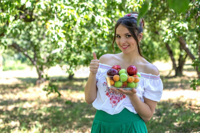 Bella ragazza che tiene un piatto di frutta e del pollice alzati su immagini stock Bella ragazza che tiene un piatto di frutta e del pollice alzati su immagini stock