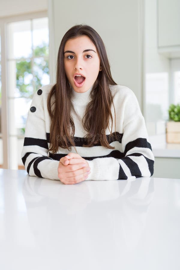 Bella ragazza con strisce maglione spaventata e scioccata dall'espressione sorpresa paura e faccia eccitata immagini stock