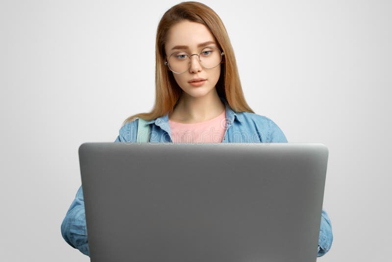 Bella ragazza dai capelli lunghi con funzionamento di vetro intento con un computer portatile Ritratto dello studio su fondo bian fotografie stock Bella ragazza dai capelli lunghi con funzionamento di vetro intento con un computer portatile Ritratto dello studio su fondo bian fotografie stock