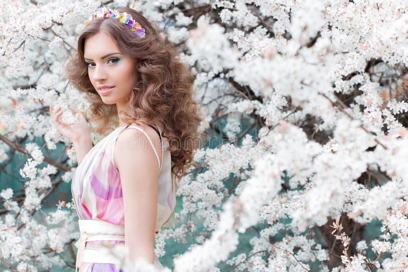 Bella ragazza elegante con capelli fertili con un orlo dei fiori brillantemente colorati in un giardino vicino ad una mattina cal immagine stock libera da diritti