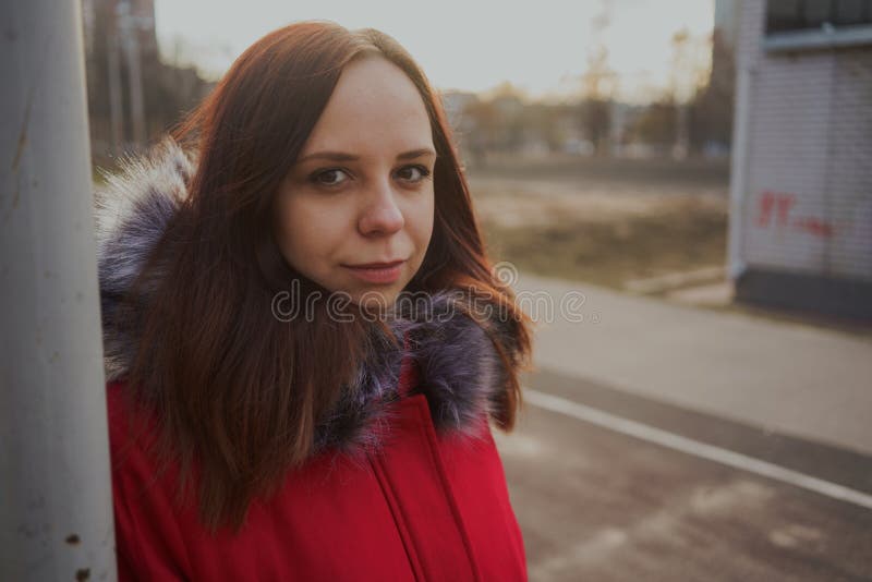 Bella ragazza felice in un rivestimento rosso che posa fuori un giorno nuvoloso fotografie stock libere da diritti Bella ragazza felice in un rivestimento rosso che posa fuori un giorno nuvoloso fotografie stock libere da diritti