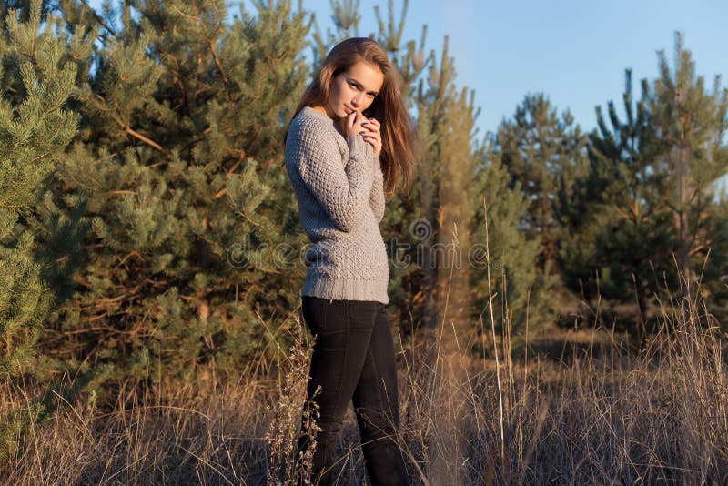 Bella ragazza sola con i grandi occhi e le ampie sopracciglia folte in un maglione caldo che cammina nella foresta al tramonto fotografia stock libera da diritti Bella ragazza sola con i grandi occhi e le ampie sopracciglia folte in un maglione caldo che cammina nella foresta al tramonto fotografia stock libera da diritti