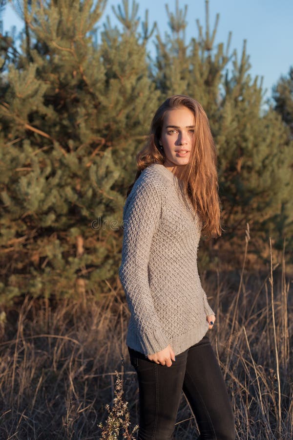 Bella ragazza sola con i grandi occhi e le ampie sopracciglia folte in un maglione caldo che cammina nella foresta al tramonto fotografia stock libera da diritti Bella ragazza sola con i grandi occhi e le ampie sopracciglia folte in un maglione caldo che cammina nella foresta al tramonto fotografia stock libera da diritti