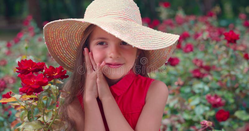 Bella ragazza sorride e rosa giardino nel parco. La donna affascinante apprezza i fiori in natura.