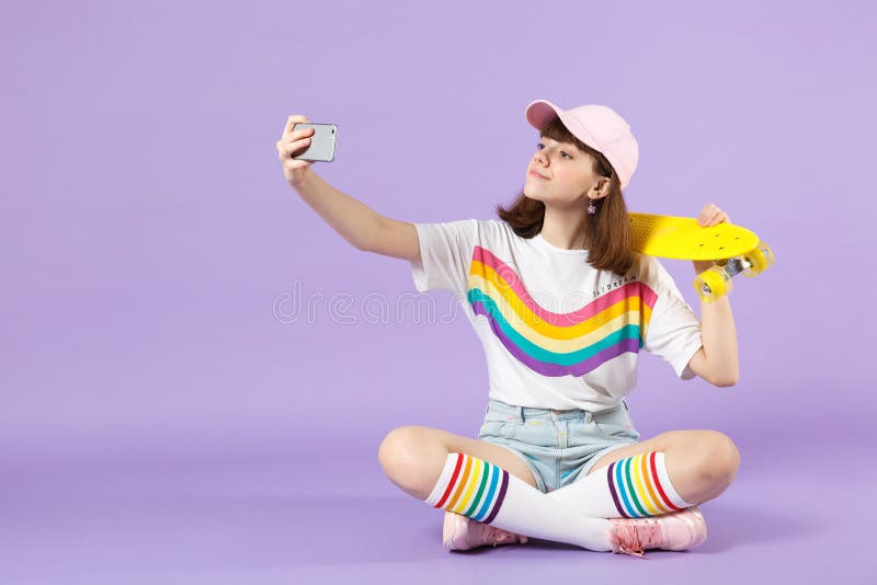 Bella ragazza teenager in vestiti vivi che tengono pattino giallo, facente selfie sparato sul telefono cellulare isolato sulla vi immagine stock libera da diritti Bella ragazza teenager in vestiti vivi che tengono pattino giallo, facente selfie sparato sul telefono cellulare isolato sulla vi immagine stock libera da diritti