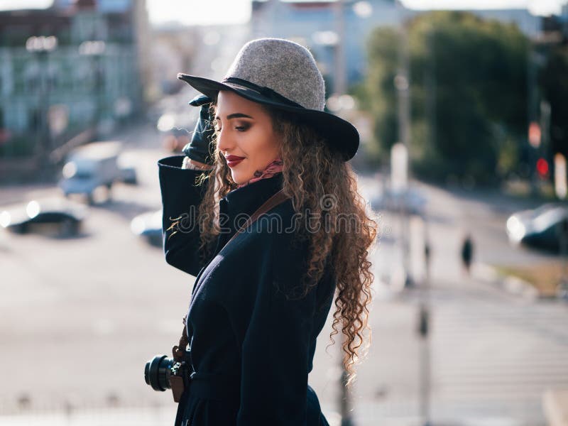 Bella ragazza in un cappotto ed in un cappello con una macchina fotografica che prende le immagini