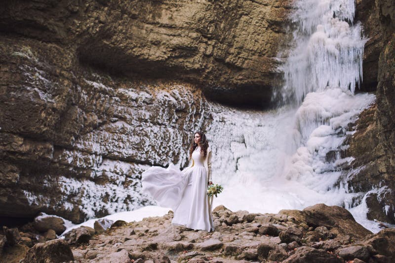 Bella ragazza in un vestito da sposa con un mazzo dei fiori su un fondo di un ghiacciaio e delle montagne immagini stock Bella ragazza in un vestito da sposa con un mazzo dei fiori su un fondo di un ghiacciaio e delle montagne immagini stock