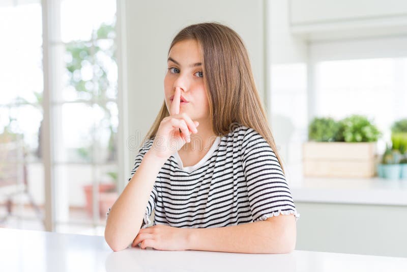Bella ragazzina con una camicia a strisce che chiede di stare tranquilla con un dito sulle labbra fotografia stock