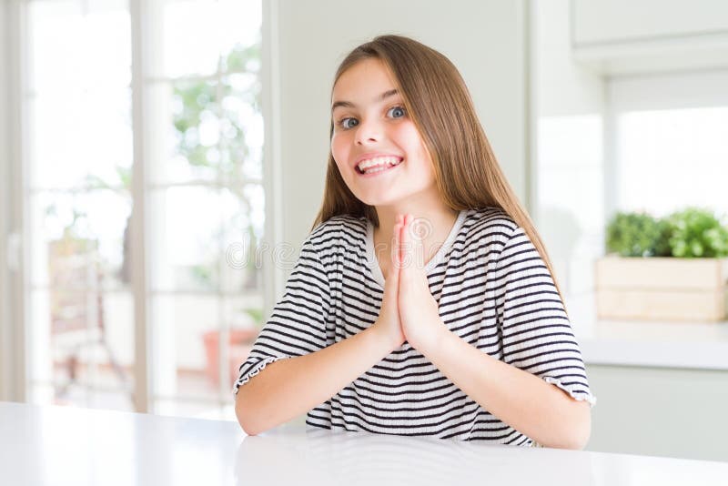 Bella ragazzina con una camicia a strisce che prega a mani nude chiedendo perdono sorridendo sicura di sé fotografia stock libera da diritti