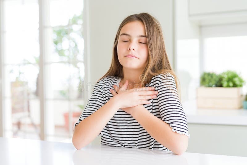 Bella ragazzina con una camicia a strisce che sorride con le mani sul petto con gli occhi chiusi e un gesto di gratitudine in facc immagini stock libere da diritti