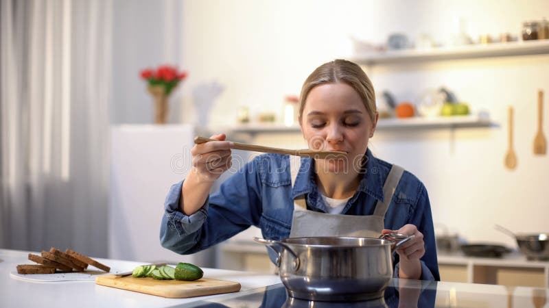 Bella signora che assaggia minestra mentre cucinando, preparando alimento per la cena, stante a dieta immagine stock Bella signora che assaggia minestra mentre cucinando, preparando alimento per la cena, stante a dieta immagine stock
