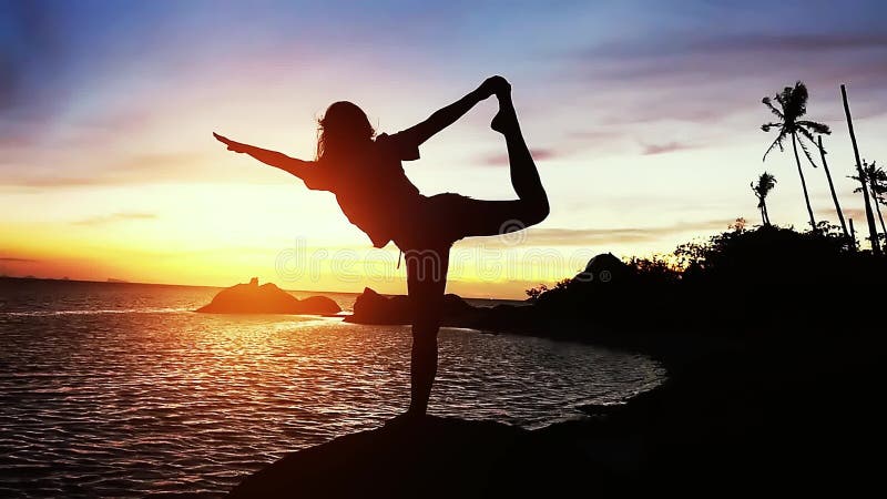 Bella vista della siluetta della giovane donna che fa yoga che allunga sulla roccia con la vista del mare al tramonto Movimento l