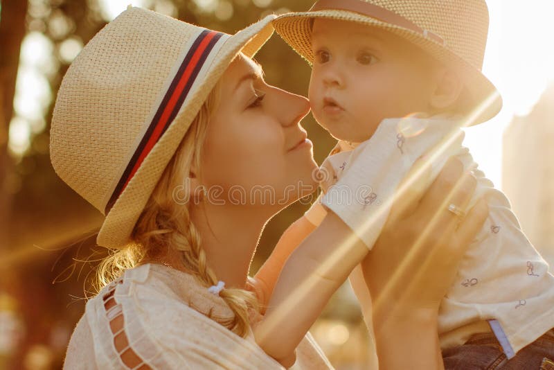 Belle blonde dans une mère de chapeau embrassant son fils au coucher du soleil en Th photographie stock Belle blonde dans une mère de chapeau embrassant son fils au coucher du soleil en Th photographie stock