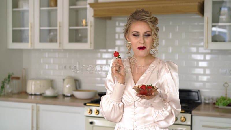 Belle chère femme mangeant des fraises dans la cuisine. banque de vidéos