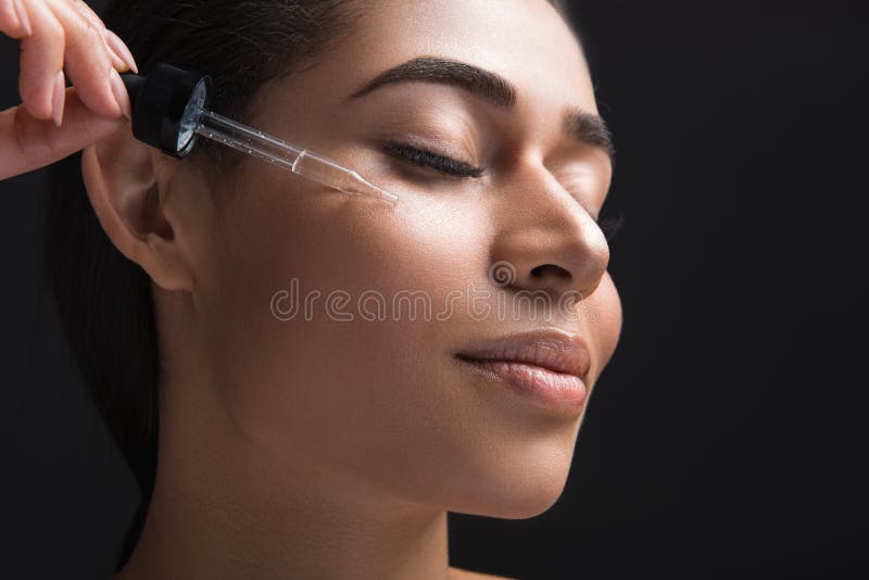 Youthfulness concept. Close up of pleased female expression with closed eyes. Woman applying serum oil on facial skin. Isolated on black background. Youthfulness concept. Close up of pleased female expression with closed eyes. Woman applying serum oil on facial skin. Isolated on black background