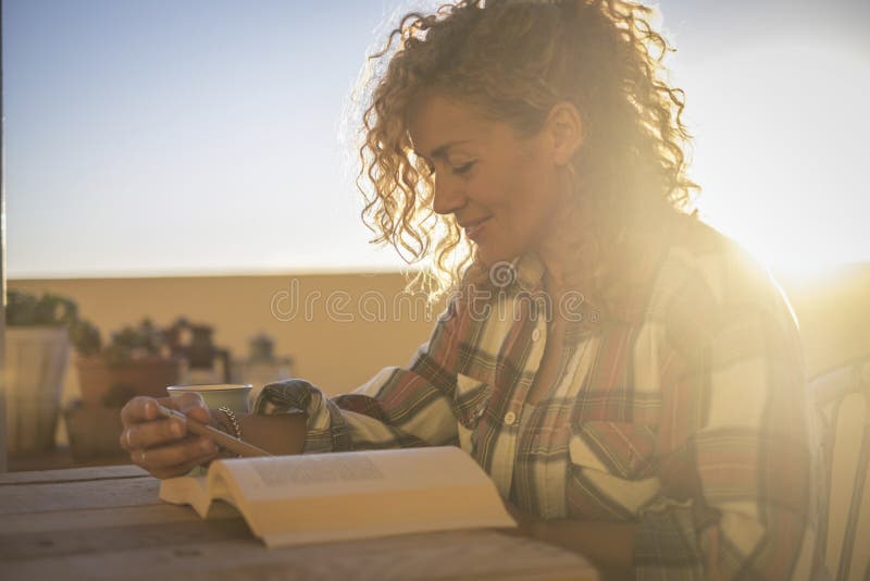 Belle et heureuse femme blonde caucasienne bouclée et souriante, en train de lire un livre qui dîne le coucher du soleil sur la t photographie stock Belle et heureuse femme blonde caucasienne bouclée et souriante, en train de lire un livre qui dîne le coucher du soleil sur la t photographie stock