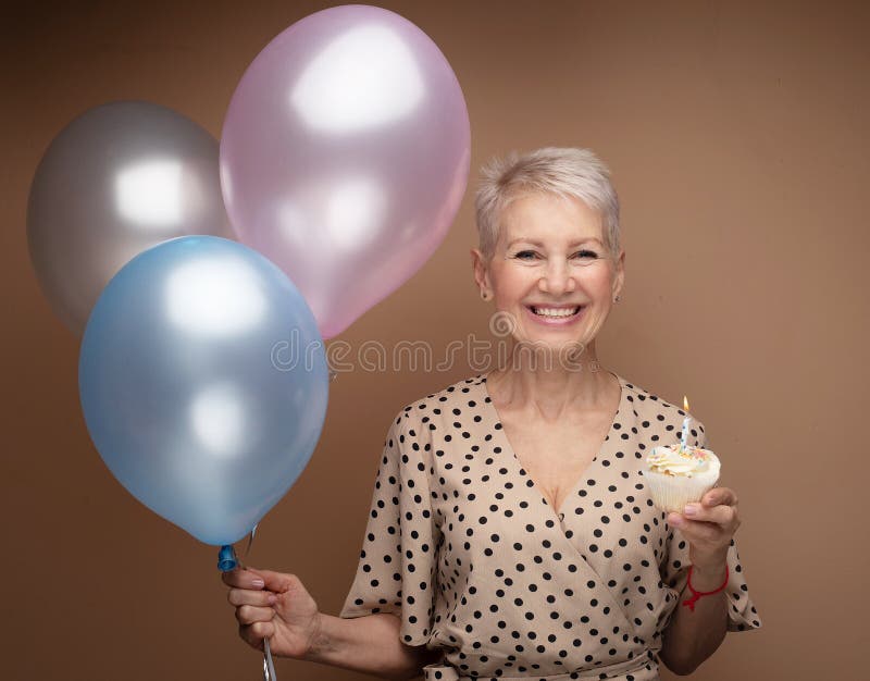 Belle femelle d'âge moyen avec cupcake avec bougie et ballon bleu dans ses mains. images stock
