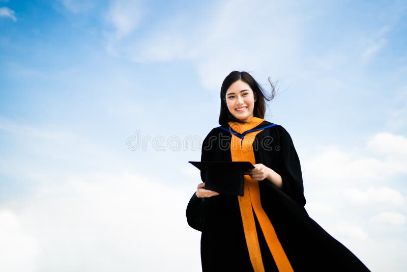 Belle femme asiatique d'étudiant de troisième cycle d'université ou d'université souriant dans la robe d'obtention du diplôme ou