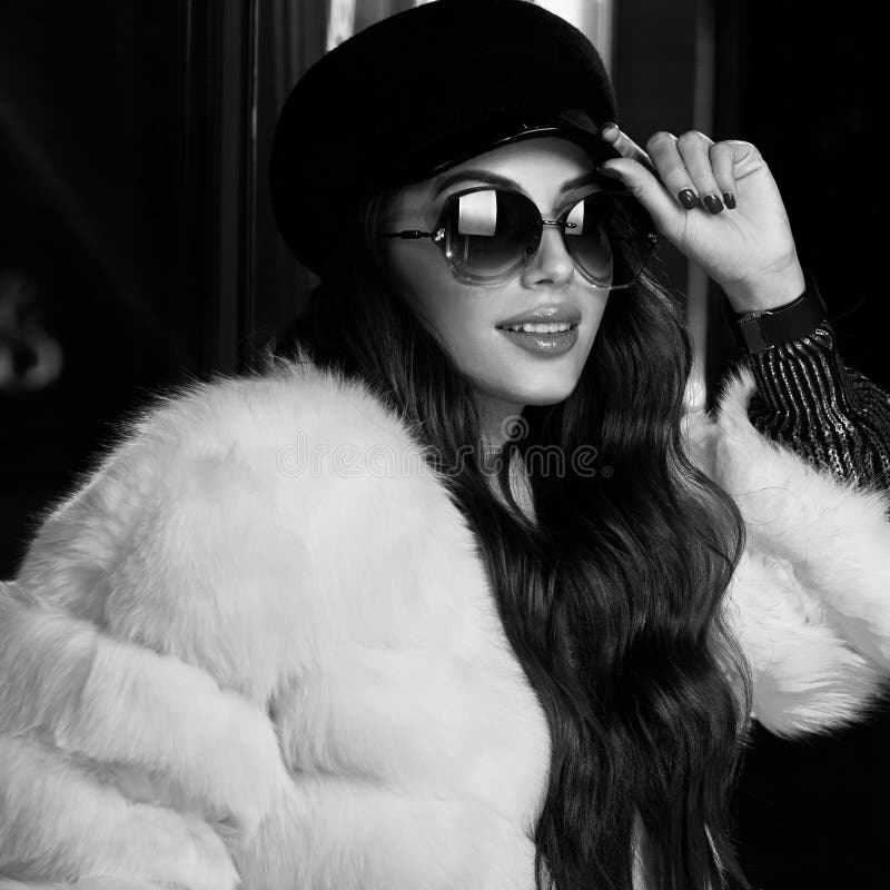 Belle femme aux cheveux longs dans le chapeau, les lunettes de soleil et le coa blanc de fourrure image libre de droits Belle femme aux cheveux longs dans le chapeau, les lunettes de soleil et le coa blanc de fourrure image libre de droits