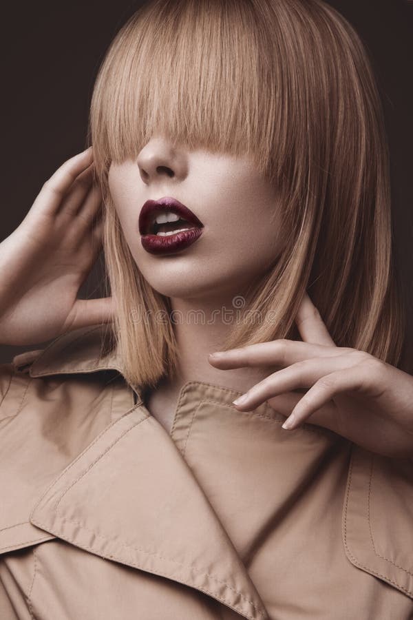 Belle femme blonde dans un manteau lumineux et des lèvres foncées, montrant différentes poses Visage de beauté photo stock Belle femme blonde dans un manteau lumineux et des lèvres foncées, montrant différentes poses Visage de beauté photo stock